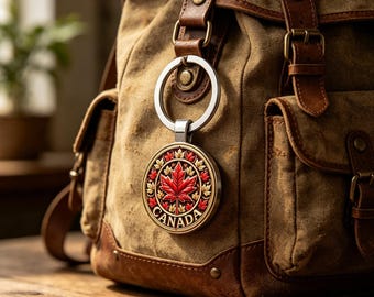 May include: A round keychain with a red maple leaf design and the word "CANADA" in red lettering. The keychain is attached to a canvas backpack with brown leather straps and accents. The background is a wooden surface.