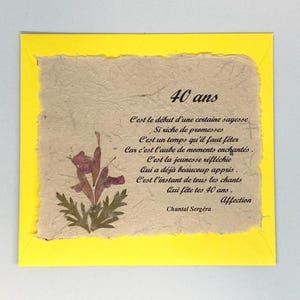 Può includere: Un biglietto di auguri fatto a mano con un bordo giallo. La carta presenta una carta beige strutturata con un fiore pressato e testo francese che celebra un 40° compleanno. Il testo include le parole "40 ans" e "Affection".
