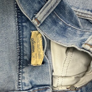 Op de afbeelding: Close-up van een blauwe spijkerbroek. Het Wrangler-label is zichtbaar, met de maat 31x36. Het label bevat wasvoorschriften. De jeans is gemaakt in de VS.