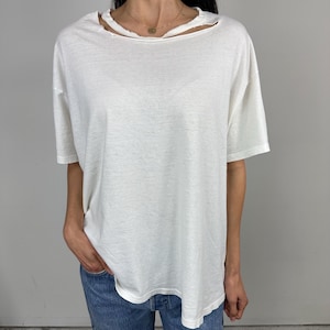 May include: White short-sleeved t-shirt with a distressed neckline. The shirt has a relaxed fit and is made of a soft, lightweight fabric. The neckline features a unique cut-out design.