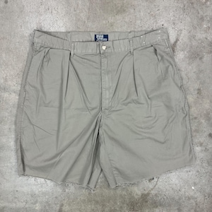 May include: Tan-colored shorts with a button closure and pleats. The shorts have a frayed hem and a small Polo logo tag. The shorts are made of a lightweight fabric.