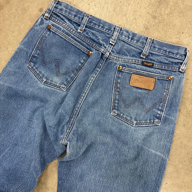 K&ouml;nnte beinhalten: Hellblaue Jeans aus Denim mit dem Wrangler-Logo auf der Ges&auml;&szlig;tasche. Die Jeans haben ein klassisches F&uuml;nf-Taschen-Design mit Messingnieten und einer verwaschenen Waschung. Die Ges&auml;&szlig;taschen haben die charakteristische Wrangler-Naht.