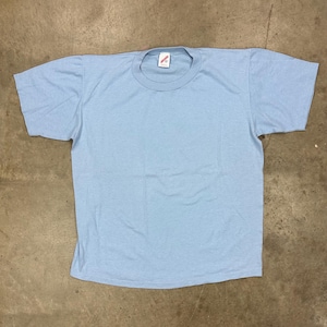 May include: A light blue, short-sleeved t-shirt, laid flat on a neutral surface. The shirt has a crew neck and a small tag at the neckline. The fabric appears to be a soft, lightweight material.