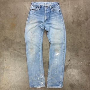 Op de afbeelding: Lichtblauwe denim jeans met een vervaagde wassing en verfspetters. De jeans hebben een klassiek ontwerp met vijf zakken, een knoop- en ritssluiting en een rechte pijp. De jeans zijn versleten en hebben distressed details.