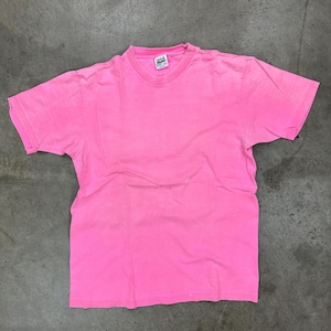 May include: A bright pink, short-sleeved t-shirt. The shirt has a crew neck and appears to be made of a soft material. The shirt is laid flat on a gray surface. The tag is visible at the back of the neck.