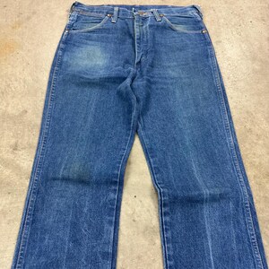 K&ouml;nnte beinhalten: Blaue Jeans aus Denim mit klassischem F&uuml;nf-Taschen-Design. Die Jeans haben einen geraden Bein-Schnitt und eine verblasste Waschung, die Gebrauchsspuren aufweist. Die Jeans liegen flach auf einer neutralen Oberfl&auml;che.