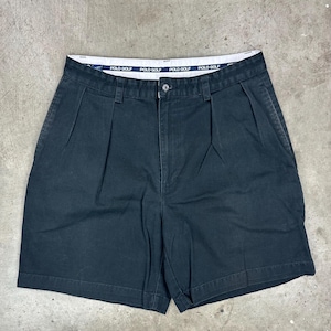 May include: Black shorts with pleats and a button closure. The waistband features the text "POLO GOLF" in white on a blue background. These shorts have pockets and a classic design.