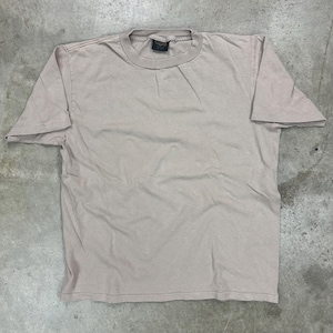 May include: A light brown, short-sleeved t-shirt. The shirt has a crew neck and a tag at the back of the neck. The fabric appears to be a soft cotton blend. The shirt is laid flat on a concrete surface.