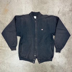 May include: A black Champion button-up jacket with a small red and white logo on the chest. The jacket has a ribbed collar, cuffs, and hem, and two front pockets. The jacket is made of a thick, soft material.