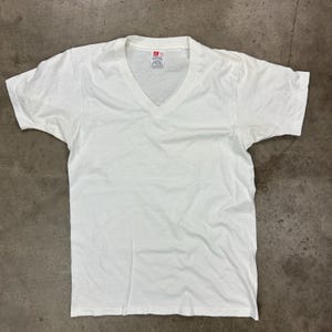 May include: A white V-neck t-shirt. The short-sleeved shirt is made of a soft, lightweight material. The shirt is laid flat on a gray surface.