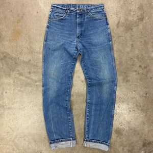 K&ouml;nnte beinhalten: Blaue Jeans aus Denim mit klassischem geradem Bein. Die Jeans haben einen Knopf- und Rei&szlig;verschluss, Vorder- und Ges&auml;&szlig;taschen sowie eine verwaschene Optik. Die Manschetten sind umgekrempelt, was auf einen Vintage-Stil hindeutet.