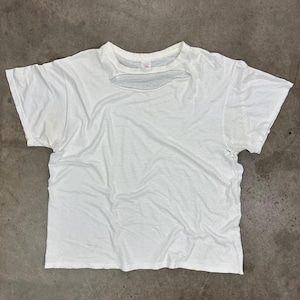 May include: A white, distressed t-shirt with a large, irregular cut-out across the chest. The shirt has short sleeves and a crew neck. The fabric appears worn and slightly stained, giving it a vintage aesthetic.