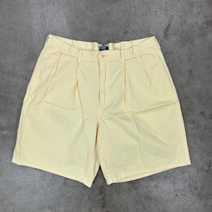 May include: Pale yellow shorts with a button closure and pleats. The shorts have a classic design and a relaxed fit. The shorts are made of a lightweight fabric and are suitable for warm weather.