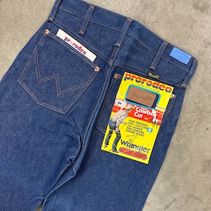 May include: Dark blue denim jeans with the Wrangler Cowboy Cut label attached. The jeans have a classic five-pocket design, copper rivets, and a "prerodeo" tag. The back pocket features the iconic "W" stitching.
