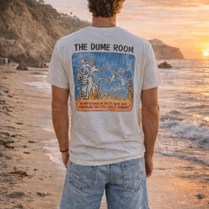 May include: A cream-coloured t-shirt featuring the text "THE DUME ROOM" above a blue rectangle with a graphic of dancing figures and flames. The text "NO MATTER WHAT WE DO TO THESE GUYS FROM MALIBU. THEY STILL CALL IT PARADISE!" is below the graphic.
