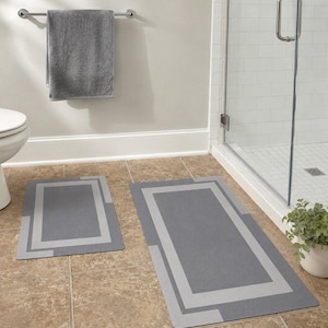 May include: A set of two rectangular bathroom rugs in a dark gray color with a lighter gray border design. The rugs feature a clean, geometric pattern with a solid center and a contrasting frame, providing a coordinated look for the bathroom floor.