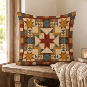 May include: A square throw pillow featuring a geometric quilt-inspired pattern with a central star motif. The design incorporates a palette of deep red, mustard yellow, muted blue, and cream, arranged in a symmetrical arrangement of triangles.