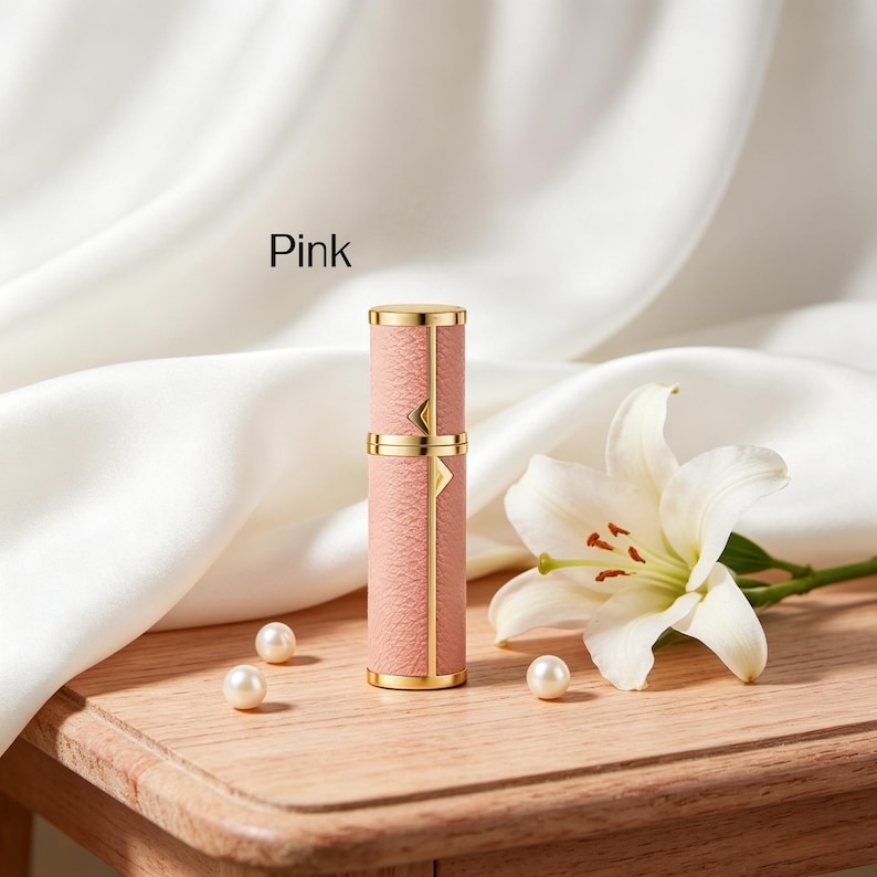 K&ouml;nnte beinhalten: Rosa Parf&uuml;mzerst&auml;uber mit goldenen Akzenten. Die zylindrische Flasche hat eine strukturierte rosa Au&szlig;enseite und goldfarbene B&auml;nder und Details. Das Wort "Pink" ist auf dem Bild aufgedruckt. Eine wei&szlig;e Lilie und Perlen sind ebenfalls im Bild.