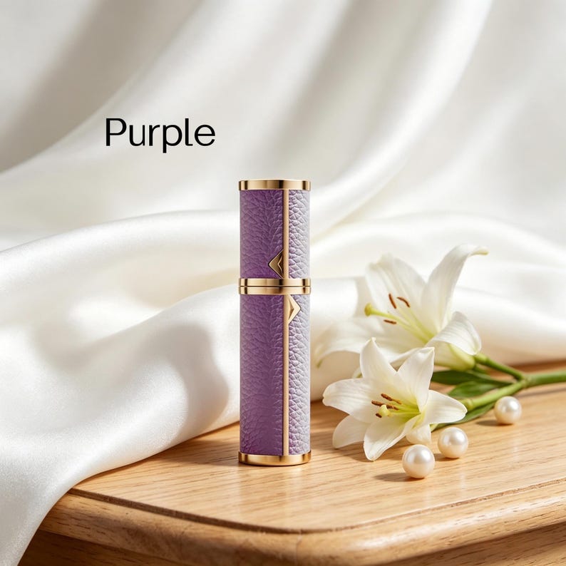 K&ouml;nnte beinhalten: Ein lila Parf&uuml;mzerst&auml;uber mit goldenen Akzenten. Der Zerst&auml;uber hat eine strukturierte, lederartige Oberfl&auml;che und ist mit "Purple" beschriftet. Der Hintergrund umfasst wei&szlig;e Lilien, Perlen und einen wei&szlig;en Satinstoff.