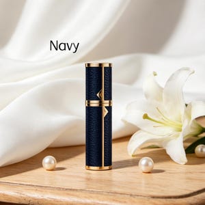 K&ouml;nnte beinhalten: Marineblauer Parf&uuml;mzerst&auml;uber mit goldenen Akzenten. Die zylindrische Flasche hat eine strukturierte Oberfl&auml;che und ist mit goldenen Zierleisten verziert. Das Wort "Navy" ist im Hintergrund aufgedruckt. Eine wei&szlig;e Lilie und Perlen sind ebenfalls im Bild.