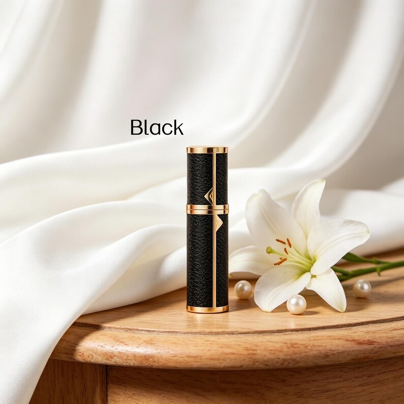 K&ouml;nnte beinhalten: Schwarzer Parf&uuml;mzerst&auml;uber mit goldenen Akzenten. Der zylindrische Beh&auml;lter hat eine strukturierte schwarze Oberfl&auml;che und goldene Verzierungen. Das Wort "Black" ist auf dem Bild aufgedruckt. Eine wei&szlig;e Lilie und Perlen sind ebenfalls im Bild.