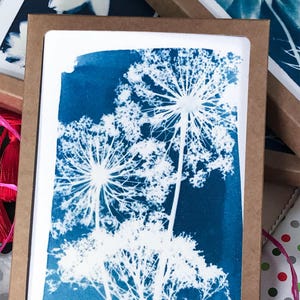 May include: A cyan blue card with a white image of three Queen Anne's Lace flowers. The card is framed in a brown cardboard frame. The text "Salon Gazelle 2014" is in the bottom left corner of the card.