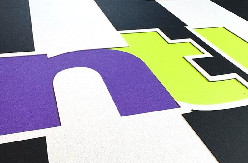 May include: Abstract composition with large, layered letters in purple, white, black, and lime green. The letters are cut out and arranged to create a dynamic, graphic design. The image has a modern, artistic feel.