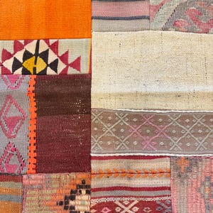 May include: Close-up of a patchwork rug with a variety of colors and patterns. The rug features rectangular and square patches in shades of orange, red, brown, gray, and cream. Geometric and floral designs are visible within the patches.
