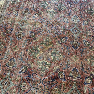 Op de afbeelding: Een groot vloerkleed met een complex, herhalend bloemen- en geometrisch patroon in tinten terracotta, gedempt blauw, saliegroen en cr&egrave;me. Het ontwerp bestaat uit onderling verbonden medaillons en krullende ranken over het gehele oppervlak.
