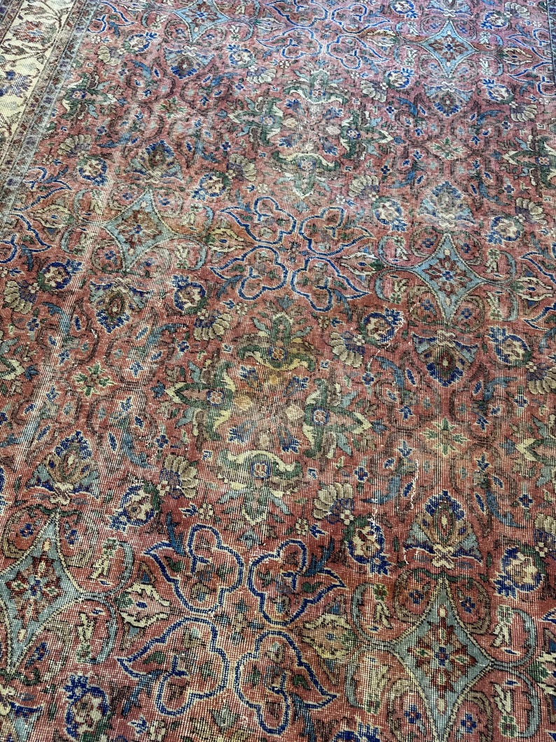 Op de afbeelding: Een groot vloerkleed met een complex, herhalend bloemen- en geometrisch patroon in tinten terracotta, gedempt blauw, saliegroen en cr&egrave;me. Het ontwerp bestaat uit onderling verbonden medaillons en krullende ranken over het gehele oppervlak.