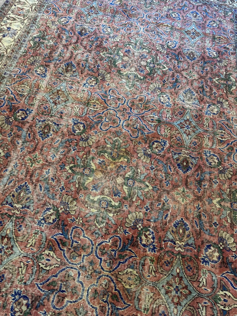 Op de afbeelding: Een groot vloerkleed met een complex, herhalend bloemen- en geometrisch patroon in tinten terracotta, saliegroen, marineblauw en cr&egrave;me. Het ontwerp bestaat uit onderling verbonden gestileerde bloesems en ranken over het gehele oppervlak.