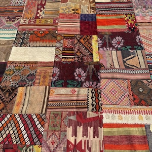 May include: A large rectangular area rug composed of various stitched fabric patches. The rug features a diverse array of woven patterns, geometric shapes, and floral motifs in a vibrant color palette including deep red, orange, brown, and cream.