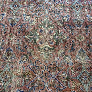 Op de afbeelding: Een geweven tapijt met een dicht, herhalend patroon van florale en geometrische motieven in tinten terracotta rood, gedempt blauw, saliegroen en cr&egrave;me. Het complexe ontwerp bestaat uit onderling verbonden medaillons en gestileerde botanische vormen.
