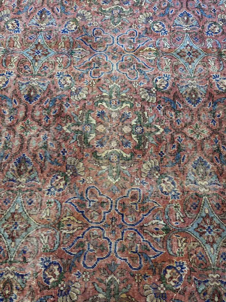 Op de afbeelding: Een geweven tapijt met een dicht, herhalend patroon van florale en geometrische motieven in tinten terracotta rood, gedempt blauw, saliegroen en cr&egrave;me. Het complexe ontwerp bestaat uit onderling verbonden medaillons en gestileerde botanische vormen.