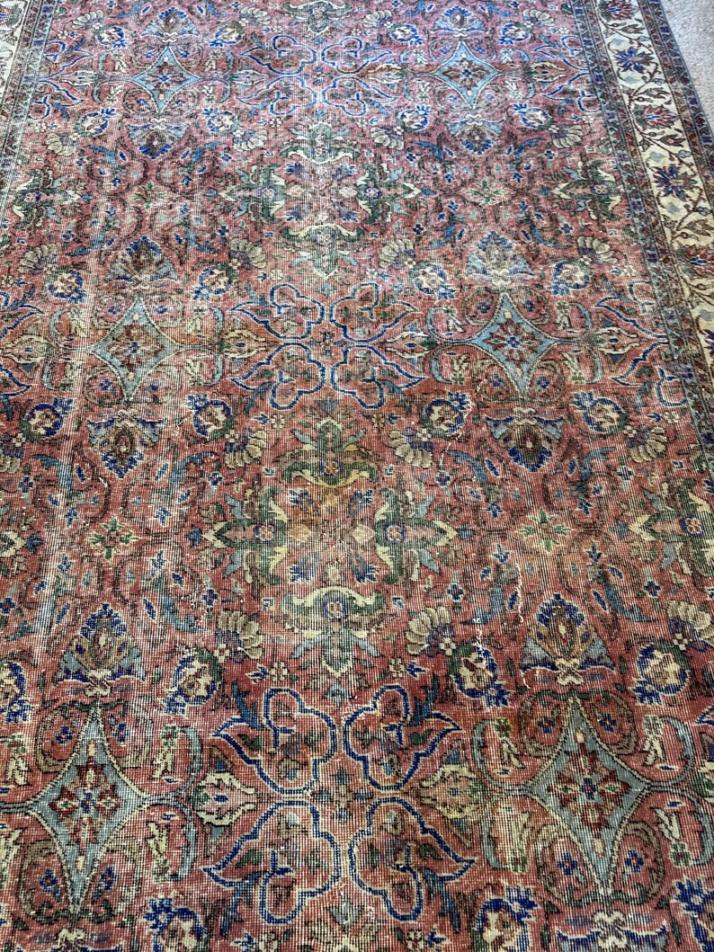 Op de afbeelding: Een rechthoekig vloerkleed met een dicht, herhalend bloemen- en geometrisch patroon in tinten terracotta, gedempt blauw, saliegroen en cr&egrave;me. Het ontwerp bevat ingewikkelde krulmotieven en een brede rand met florale elementen.