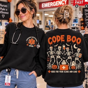 May include: A black crewneck sweatshirt featuring a small orange star of life emblem on the front left chest with the text Emergency Department and Sophia. The back displays four skeletons, ghosts, pumpkins, and the text Code Boo Here For Your Scare And Care.