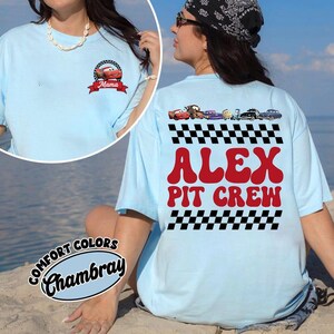 May include: A light blue t-shirt featuring a small graphic on the front chest of a red race car with the text Mama. The back displays a row of colorful race car characters above a checkered pattern, the red text ALEX PIT CREW, and another checkered pattern.