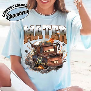 K&ouml;nnte beinhalten: Hellblaues T-Shirt mit einer Grafik von Hook aus dem Film Cars. Das Wort "MATER" ist im Used-Look &uuml;ber der Grafik aufgedruckt. Das Shirt tr&auml;gt auch die Worte "COMFORT COLORS Chambray" auf der oberen linken Seite.