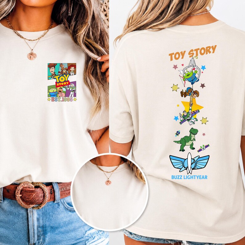 May include: A cream-colored t-shirt featuring Toy Story graphics. The front displays a small square print with characters and the text "TOY STORY EST. 1995". The back features a vertical design with characters, stars, and "TOY STORY" and "BUZZ LIGHTYEAR" text.