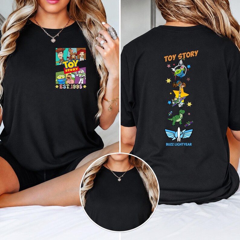May include: A black t-shirt featuring a small Toy Story graphic on the left chest with the text EST. 1995. The back of the shirt displays a vertical design with Toy Story characters, stars, and the text TOY STORY and BUZZ LIGHTYEAR at the bottom.