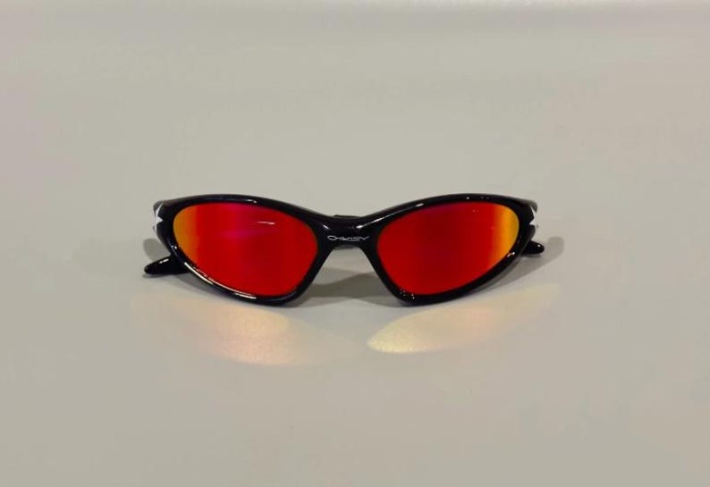 May include: Black sunglasses with red lenses. The sunglasses have a sleek, curved design with a glossy black frame. The lenses have a gradient effect, transitioning from red to orange.