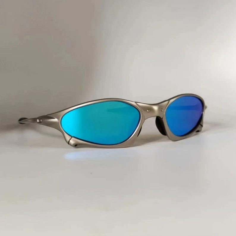 May include: Silver-framed sunglasses with blue mirrored lenses. The sunglasses have a sleek, modern design with a curved frame and a subtle nose bridge. The lenses reflect a vibrant blue hue, offering a stylish and functional accessory.
