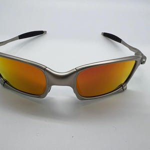 Puede incluir: Gafas de sol con montura plateada y lentes naranjas y amarillas. Las gafas de sol tienen un dise&ntilde;o elegante y moderno con una montura curvada y puntas de patillas negras. Las lentes ofrecen un degradado de color.
