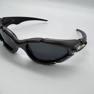 Könnte beinhalten: Schwarze Sonnenbrille mit Wrap-around-Design. Die Sonnenbrille hat eine dunkle Tönung und eine moderne Ästhetik. Die Fassung ist mattschwarz, die Bügel sind gebogen. Geeignet für Outdoor-Aktivitäten und bietet Sonnenschutz.