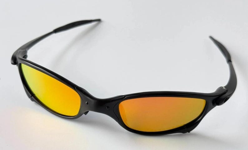 May include: Black sunglasses with orange-yellow lenses. The sunglasses have a sleek, sporty design with a black frame and curved temples. The lenses have a gradient effect, transitioning from yellow to orange.
