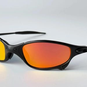 May include: Black sunglasses with orange and yellow gradient lenses. The sunglasses have a sleek, curved design with a black frame and arms. The lenses transition from yellow to orange, creating a vibrant look.
