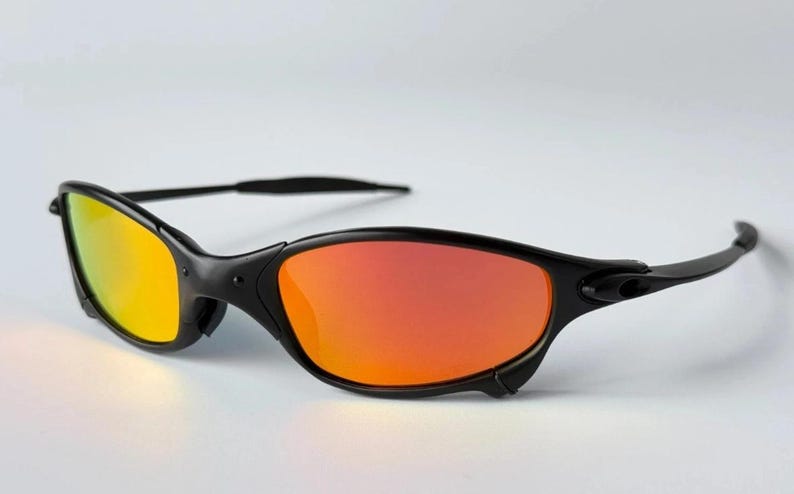 May include: Black sunglasses with orange and yellow gradient lenses. The sunglasses have a sleek, curved design with a black frame and arms. The lenses transition from yellow to orange, creating a vibrant look.