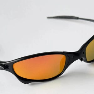 May include: Black sunglasses with orange and yellow gradient lenses. The sunglasses have a sleek, sporty design with a curved frame and temples. The lenses are a vibrant orange color, transitioning to yellow.