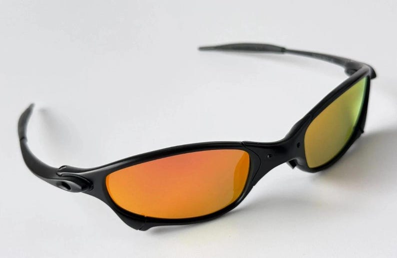 May include: Black sunglasses with orange and yellow gradient lenses. The sunglasses have a sleek, sporty design with a curved frame and temples. The lenses are a vibrant orange color, transitioning to yellow.