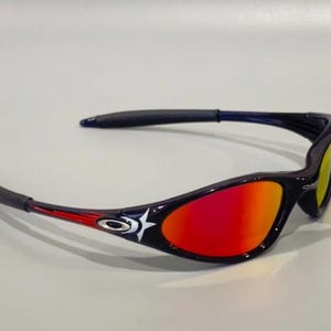 May include: Sport sunglasses with a black frame, red and yellow gradient lenses, and a white star design. The arms have red accents. These sunglasses are designed for outdoor activities and offer UV protection.